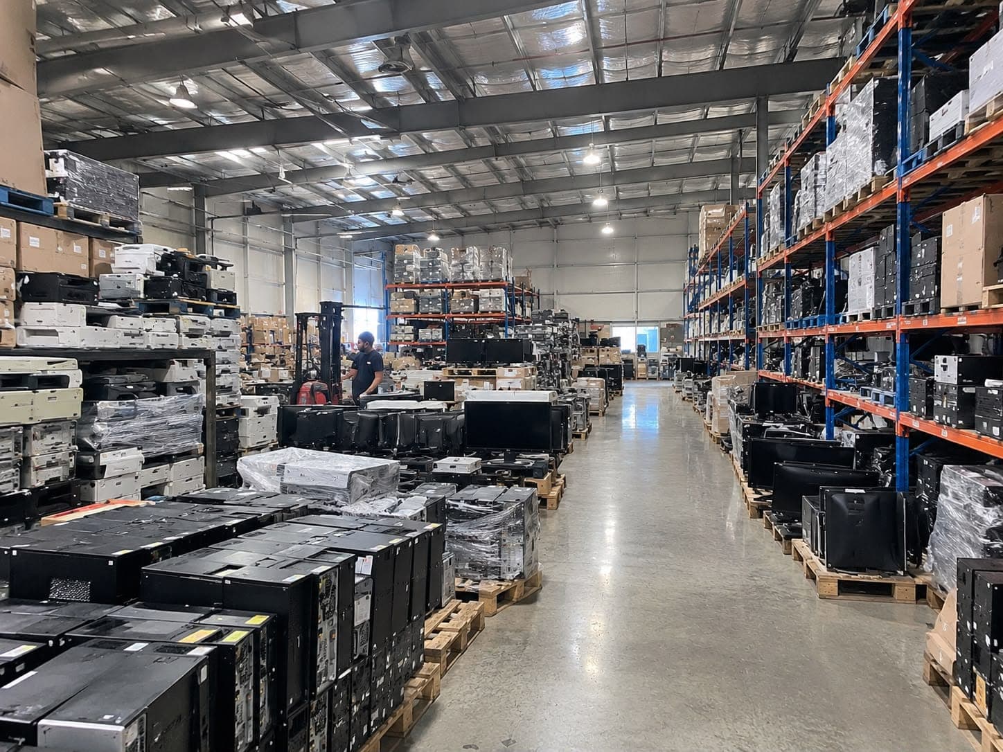 The MGE warehouse floor, with pallets of desktop towers and monitors and a forklift at work